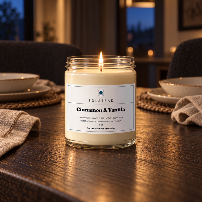 Solstead Cinnamon & Vanilla 9 oz soy candle burning on a dark wooden dining table set for dinner