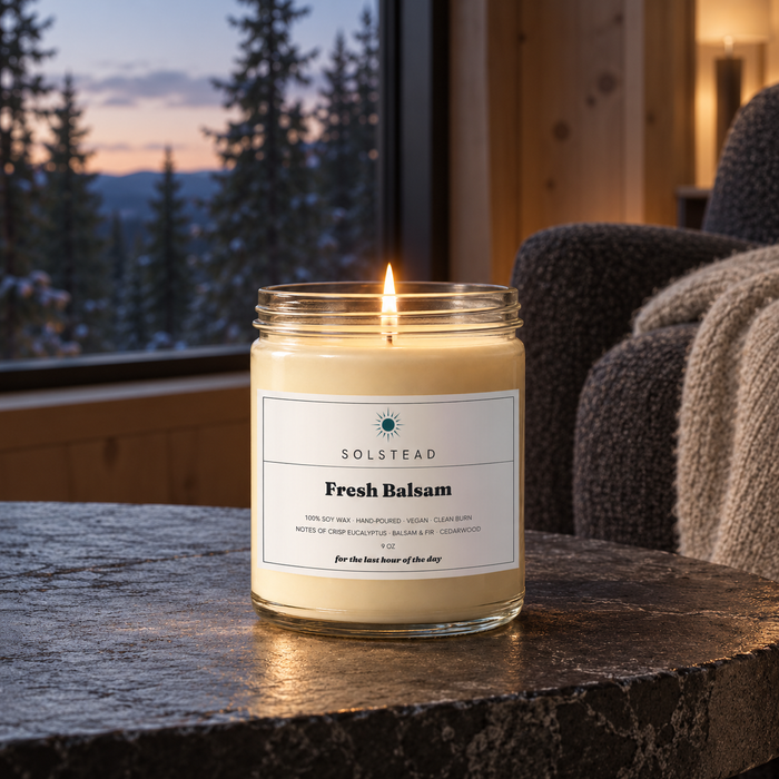 Solstead Fresh Balsam 9 oz soy candle burning on a stone table by a window with pine trees at dusk