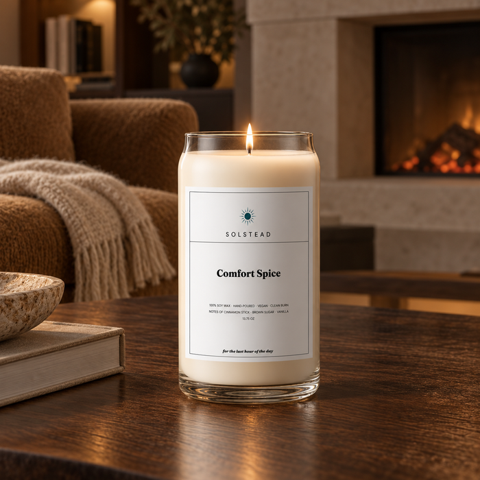 Solstead Comfort Spice 13.75 oz soy candle burning on a dark wooden coffee table in front of a fireplace