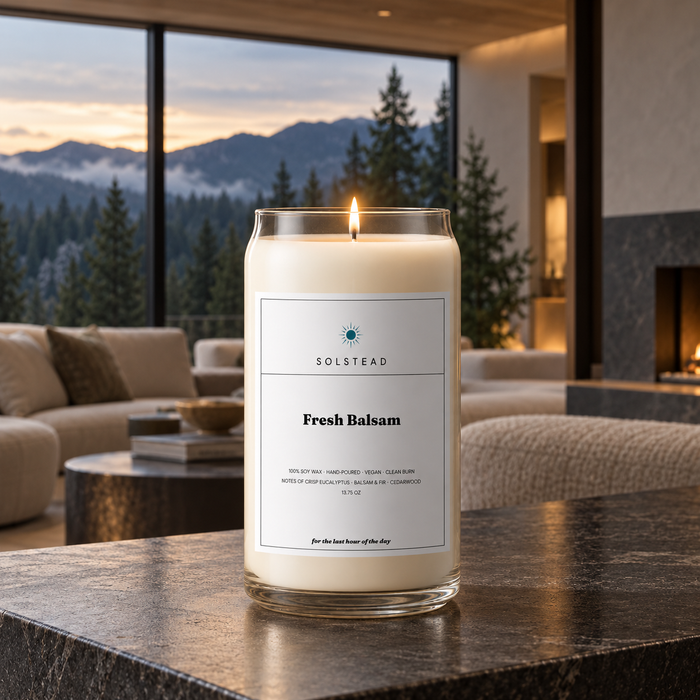 Solstead Fresh Balsam 13.75 oz soy candle burning on a dark stone table in a living room with a mountain and forest view