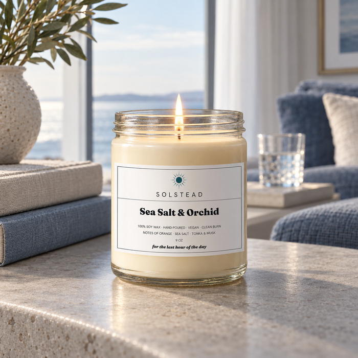 Solstead Sea Salt & Orchid 9 oz soy candle burning on a stone table by a window with a view of the water