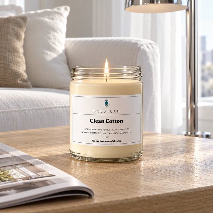 Solstead Clean Cotton 9 oz soy candle burning on a side table beside a white sofa and an open magazine