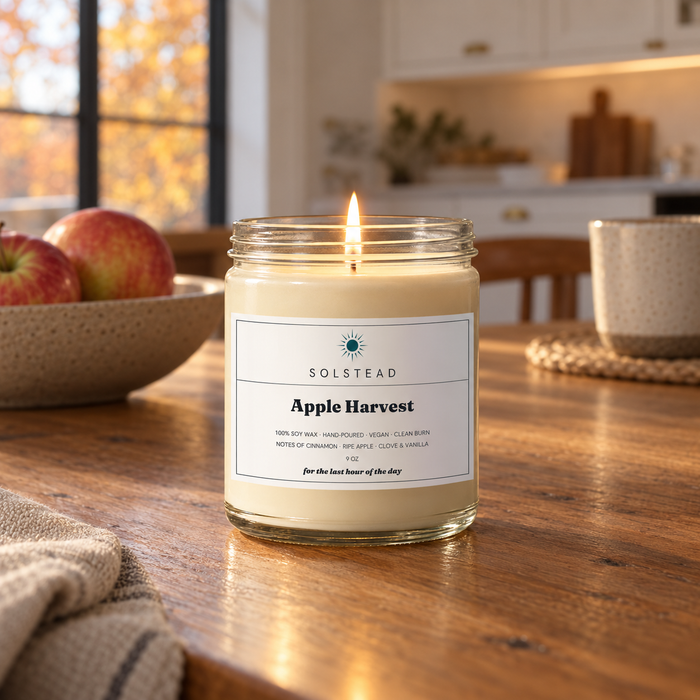 Solstead Apple Harvest 9 oz soy candle burning on a wooden kitchen table beside a bowl of apples