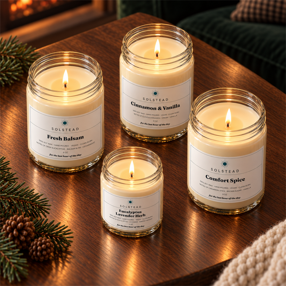 The Christmas Set by Solstead seen from above: the three 9 oz candles and the 4 oz candle burning on a wooden table with pine sprigs and a knit throw